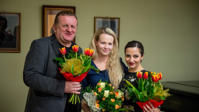 dwie kobiety i mężczyzna z bukietami kwiatów w rękach