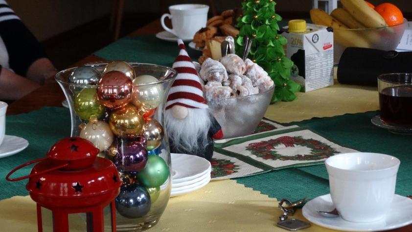 Stół, na którym znajdują się elementy wystroju bożonarodzeniowego: mała choinka, lampion i bańki w szklanym naczyniu.