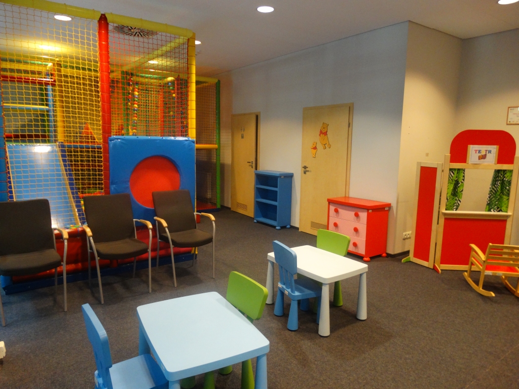 Sala zabaw dla najmłodszych. na pierwszym planie dwa malutkie stoliki z kolorowymi krzesełkami, w głebi suchy basen