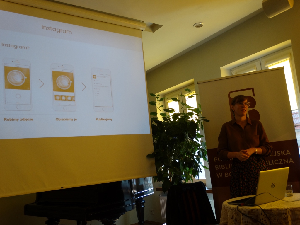 Dominika Drobiazg stojąca przed ekranem laptopa w tle ekran z prezentacją multimedialną