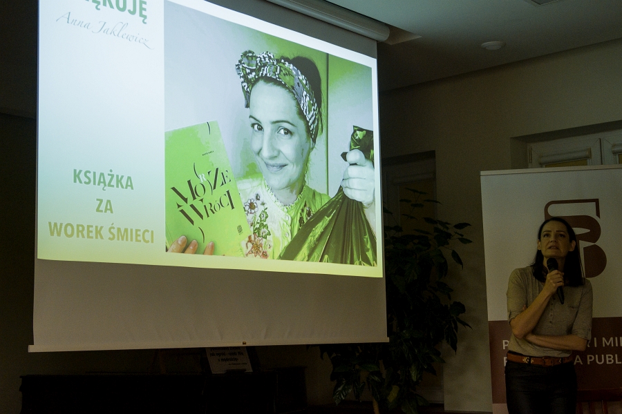 ekran ,na którym znajduje sie slajd z tekstem Książka za worek śmieci oraz fotografia Anny Jaklewicz. Prelegentka stoi obok w prawej rece trzyma mikrofon