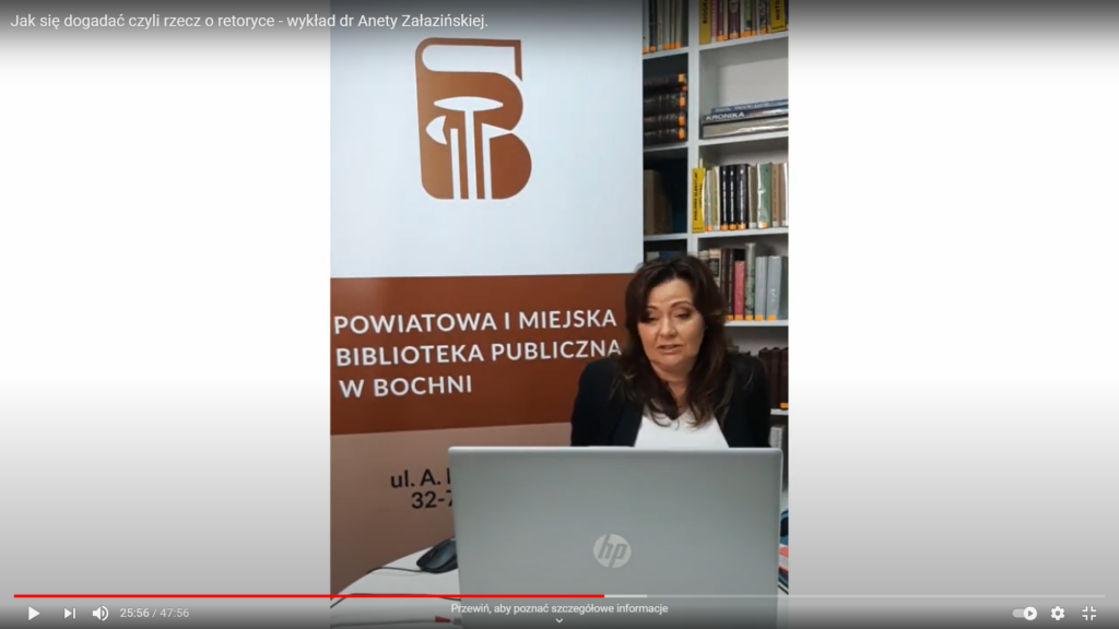 Dr hab. Aneta Załazińska spoglądająca w ekran laptopa na tle banera z logo biblioteki