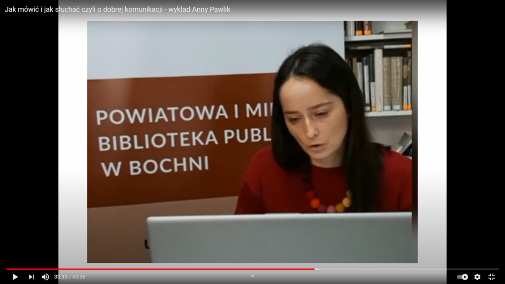 Anna Pawlik spoglądająca w ekran laptopa. W tle baner z logo biblioteki.