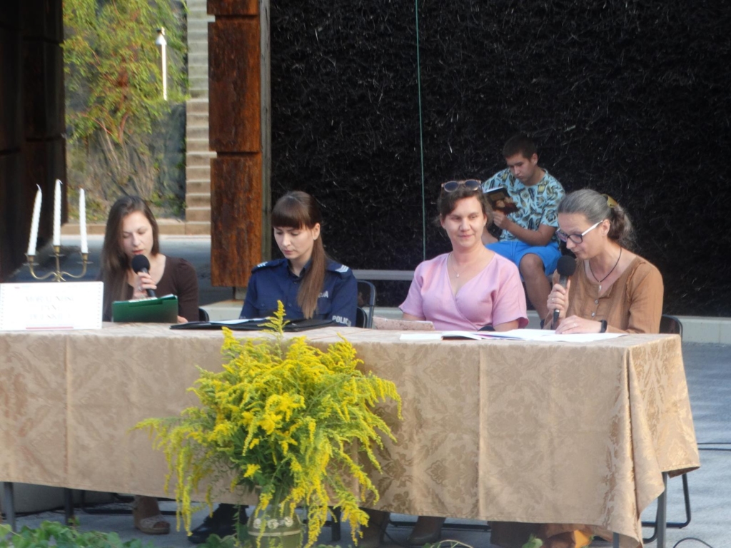 cztery czytające kobiety siedzące za duzym stołem Na pierwszym planie wazon z kwiatami