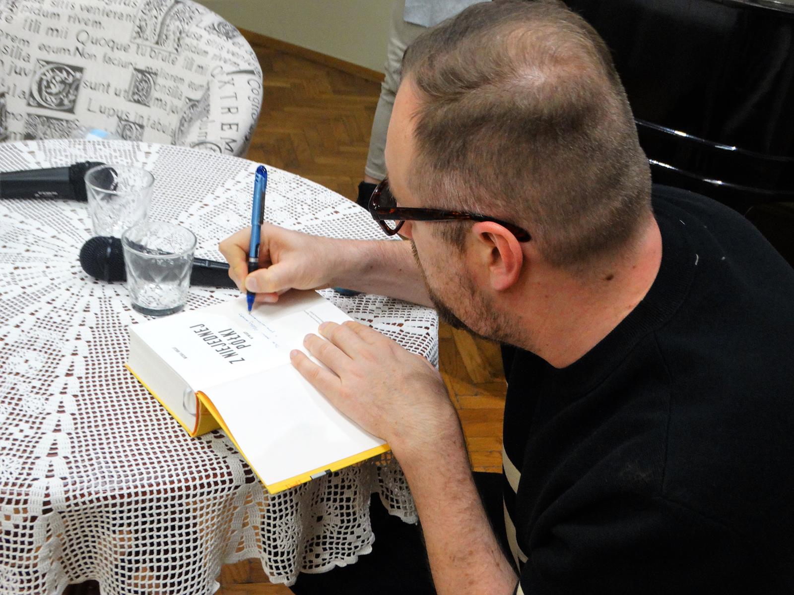 Redaktor Michał Nogaś wpisuje dedykacje do swojej książki