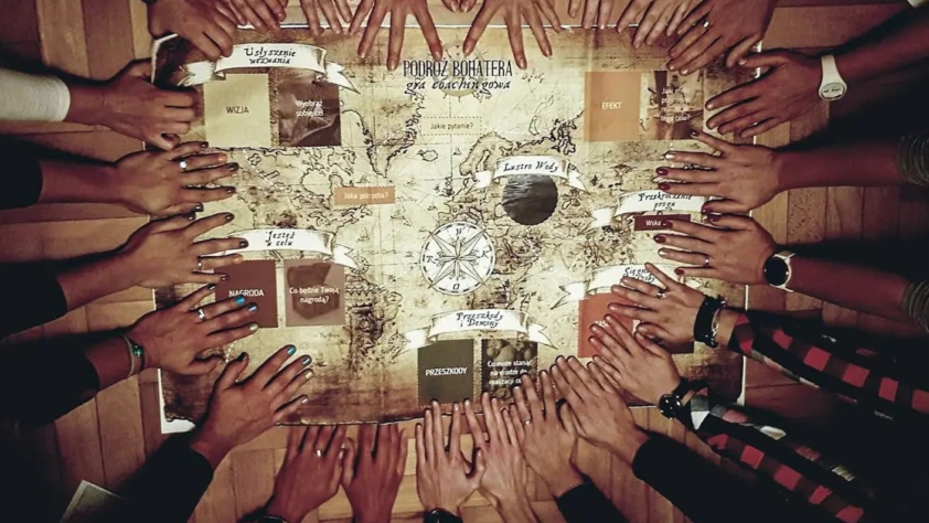 plakat obrazujący dłonie na stole, zapowiada grę bohatera